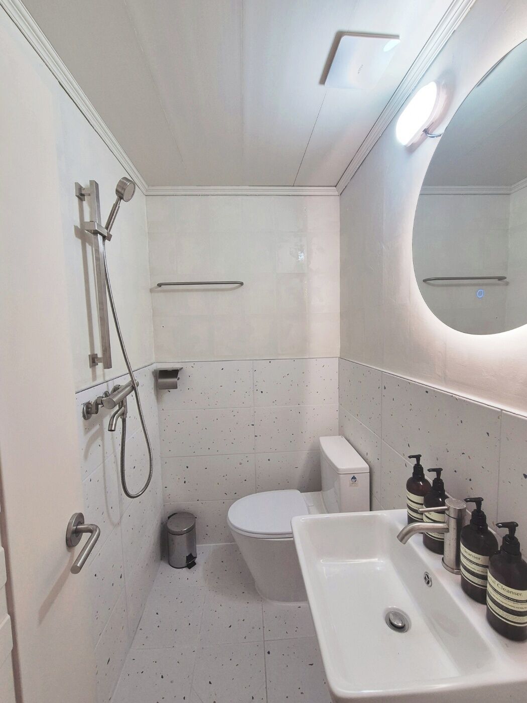 A modern bathroom with a white sink, toilet, and shower area. There are two soap dispensers on the sink.