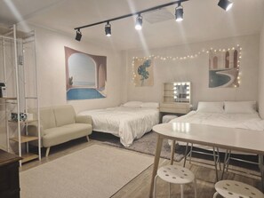 Quarto com duas camas, uma escrivaninha, uma cadeira, toucador iluminado, uma janela grande e uma planta.