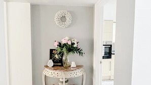 A hallway with a white console table featuring a welcome sign, a vase with flowers, and decorative items.