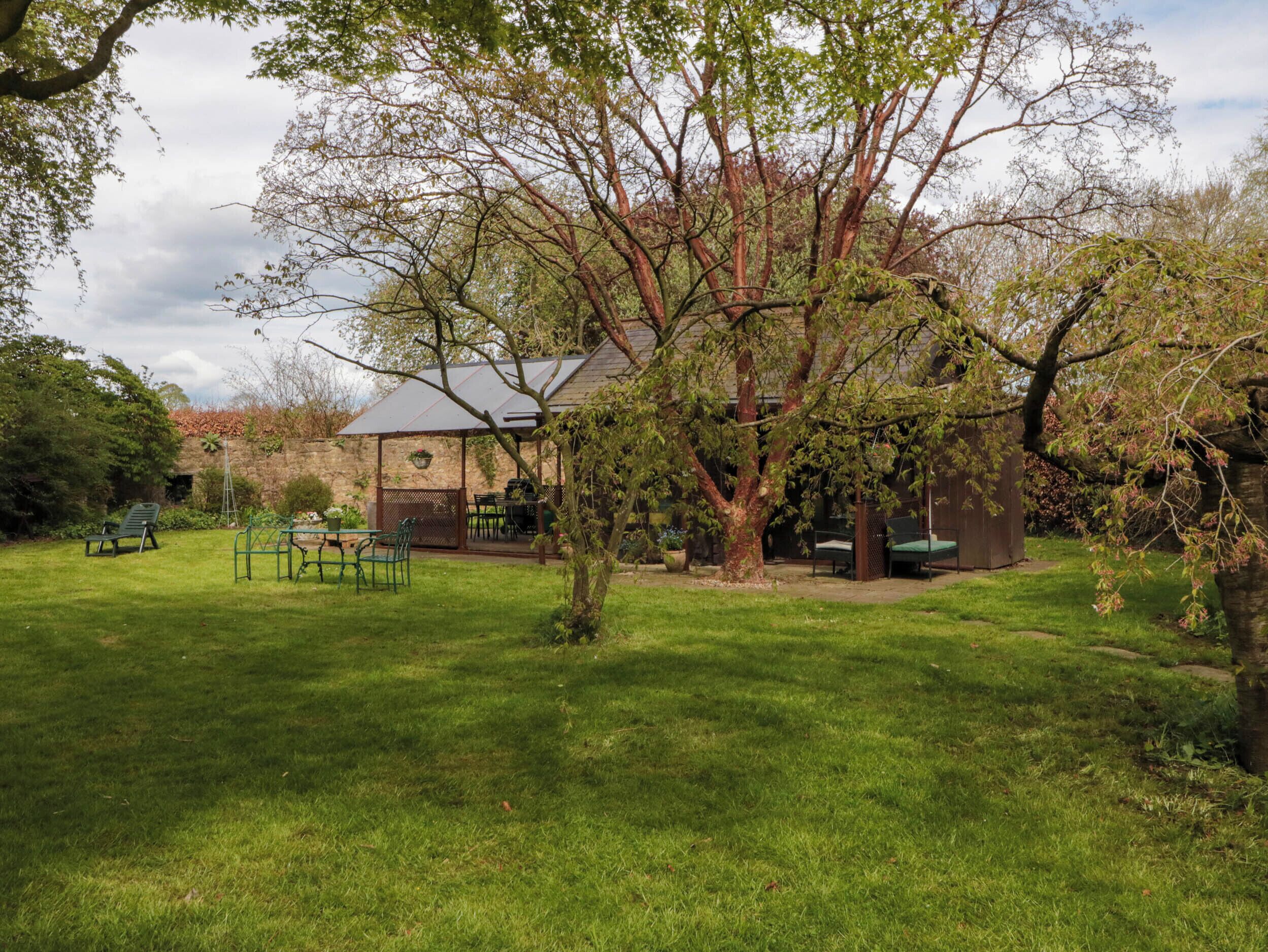 A rustic house with a garden patio, a stone wall, and a large tree.
