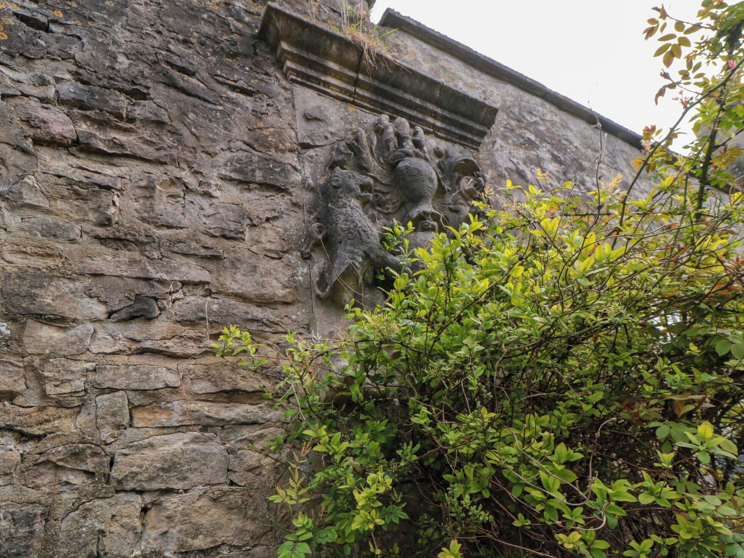 Eine Steinsäule mit einem in Stein gemeißelten Löwenkopf und Vegetation im Vordergrund.