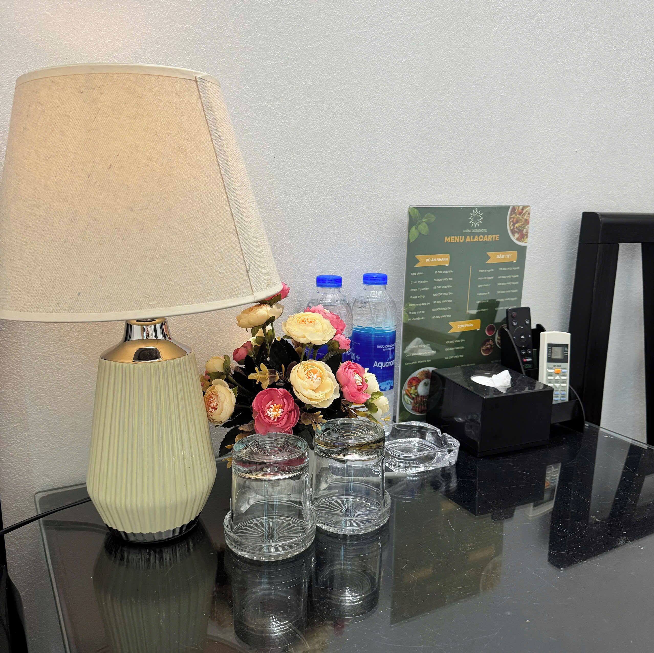 Una mesa con una lámpara, una composición floral, botellas de agua, un menú y una caja de pañuelos.