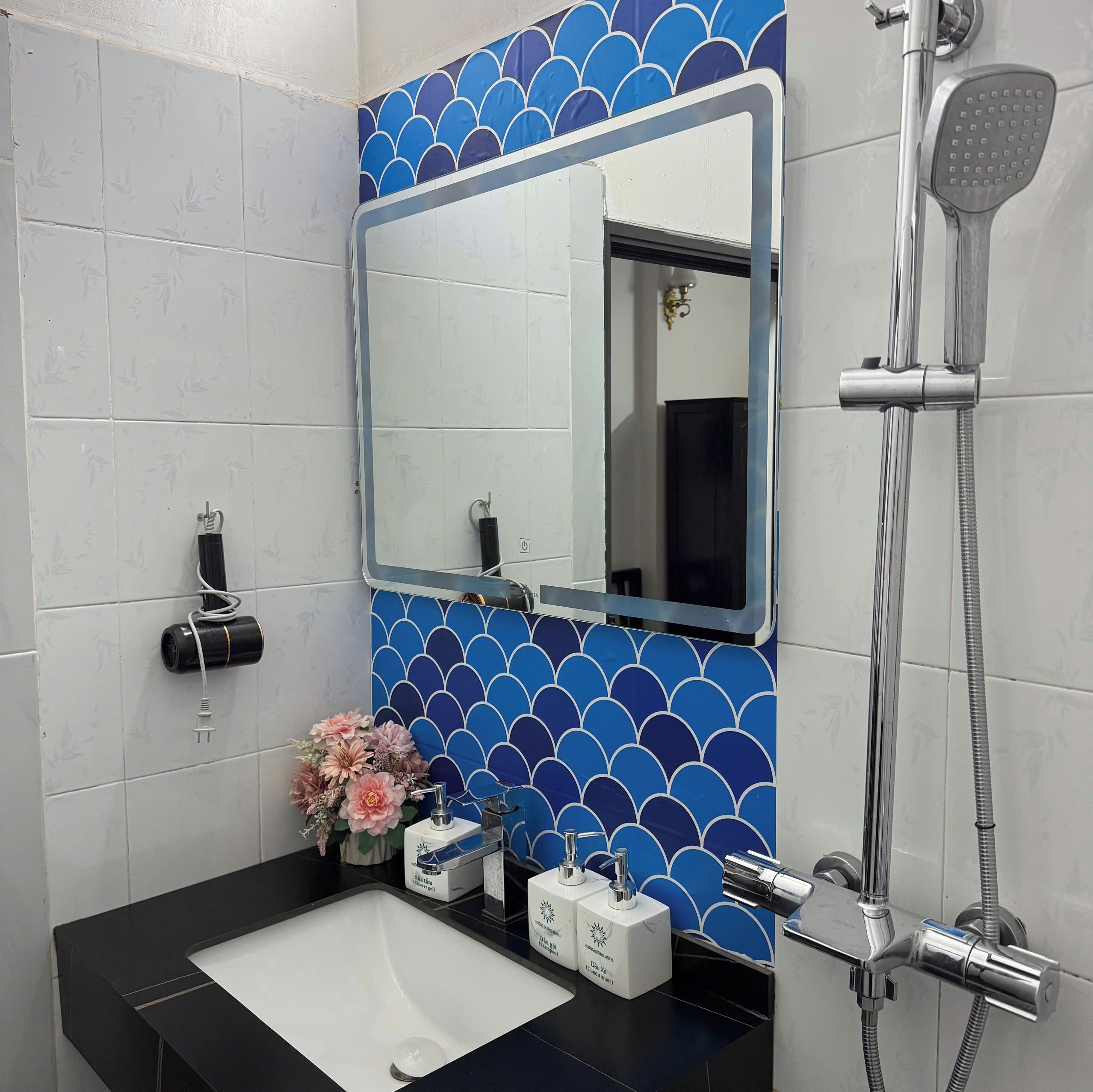 Un baño con un lavamanos blanco, un espejo, una ducha y una pared con azulejos azules.