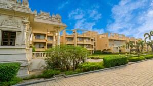 A modern hotel with a traditional architectural style, featuring a courtyard with greenery and palm trees. - Jagriti Dham (Alipur)