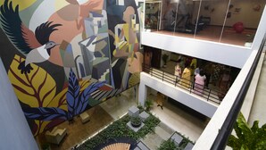 A multi-level atrium with a large mural, a staircase, and a seating area with plants. - Jagriti Dham (Alipur)