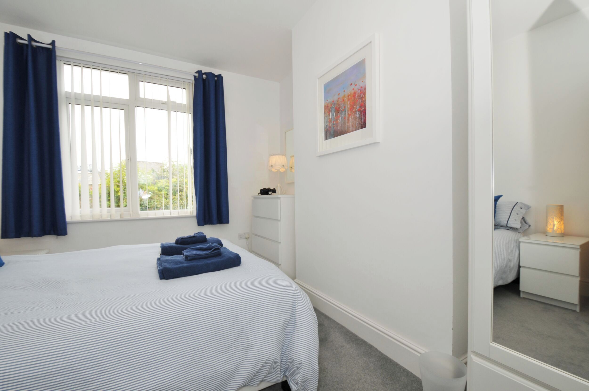 A bedroom with a bed, a nightstand, a lamp, and a painting on the wall.