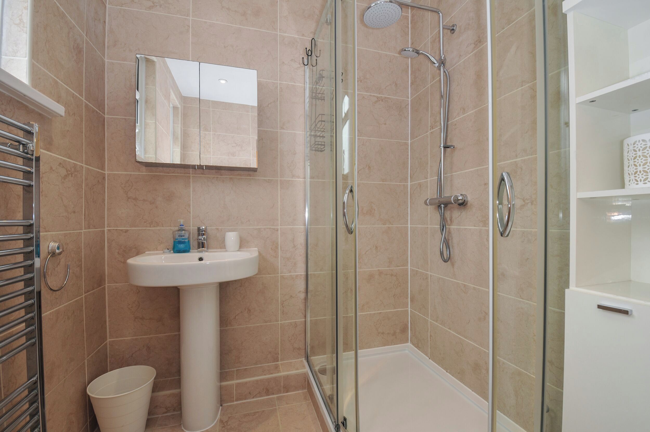 A modern bathroom with a glass-enclosed shower, a pedestal sink, and a mirrored cabinet.