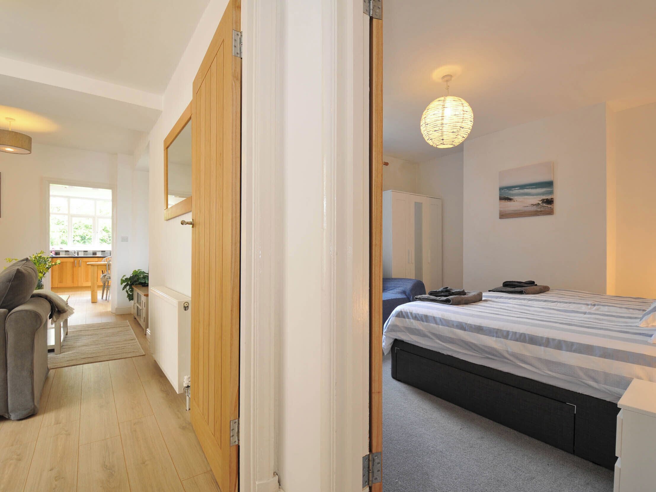 A bedroom with a bed, a bedside table, a lamp, a wardrobe, and a view of the kitchen.