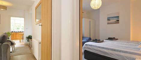 A bedroom with a bed, a bedside table, a lamp, a wardrobe, and a view of the kitchen.