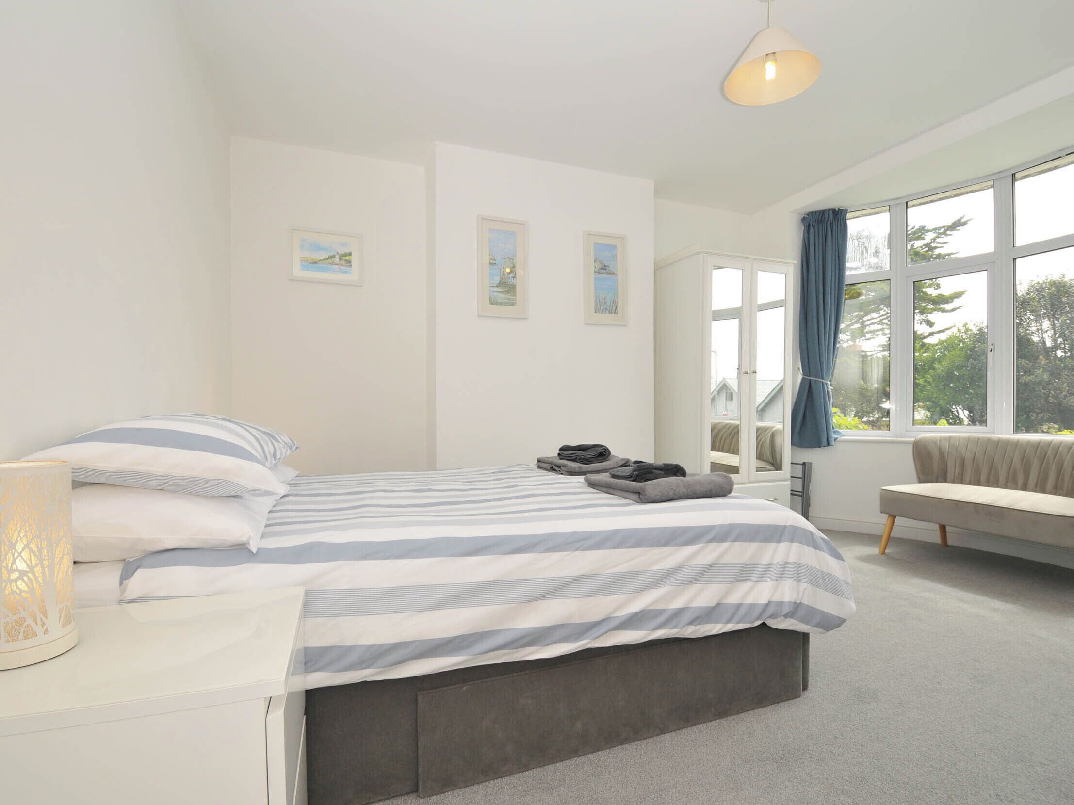 A modern bedroom with a large bed, a bedside lamp, a bench, and a view of the outdoors through a window.