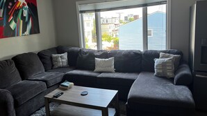 A living room with a sectional sofa, a coffee table, and a painting on the wall. - Charming 2-bedroom condo in delightful Chelsea with WiFi, AC (Chelsea)