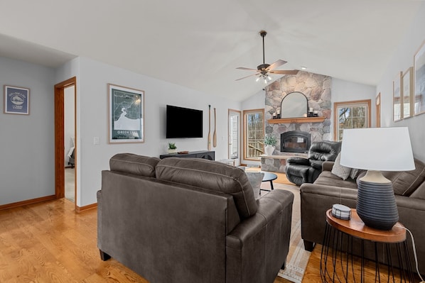 A living room with a stone fireplace, leather sofas, a television, and a ceiling fan.