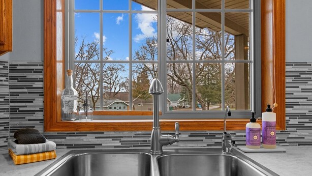 A kitchen with a double sink, a window with a view of trees and houses, and two bottles of soap on the counter. - Oak Haven Retreat, Oak Haven Retreat  - Charming Green Lake Property (Princeton)
