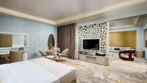 A hotel room with a large bed, a desk with a chair, a TV, a sofa, and a decorative wall panel. - Avenra Garden (Negombo)