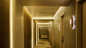 A long, narrow hotel corridor with a carpeted floor, wooden panel walls, and doors with light fixtures. - Avenra Garden (Negombo)
