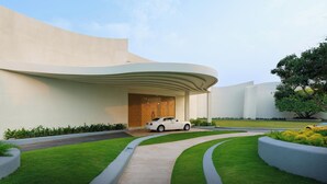 A modern building with a curved entrance, a white car parked in front, and a well-maintained lawn with pathways. - Avenra Garden (Negombo)