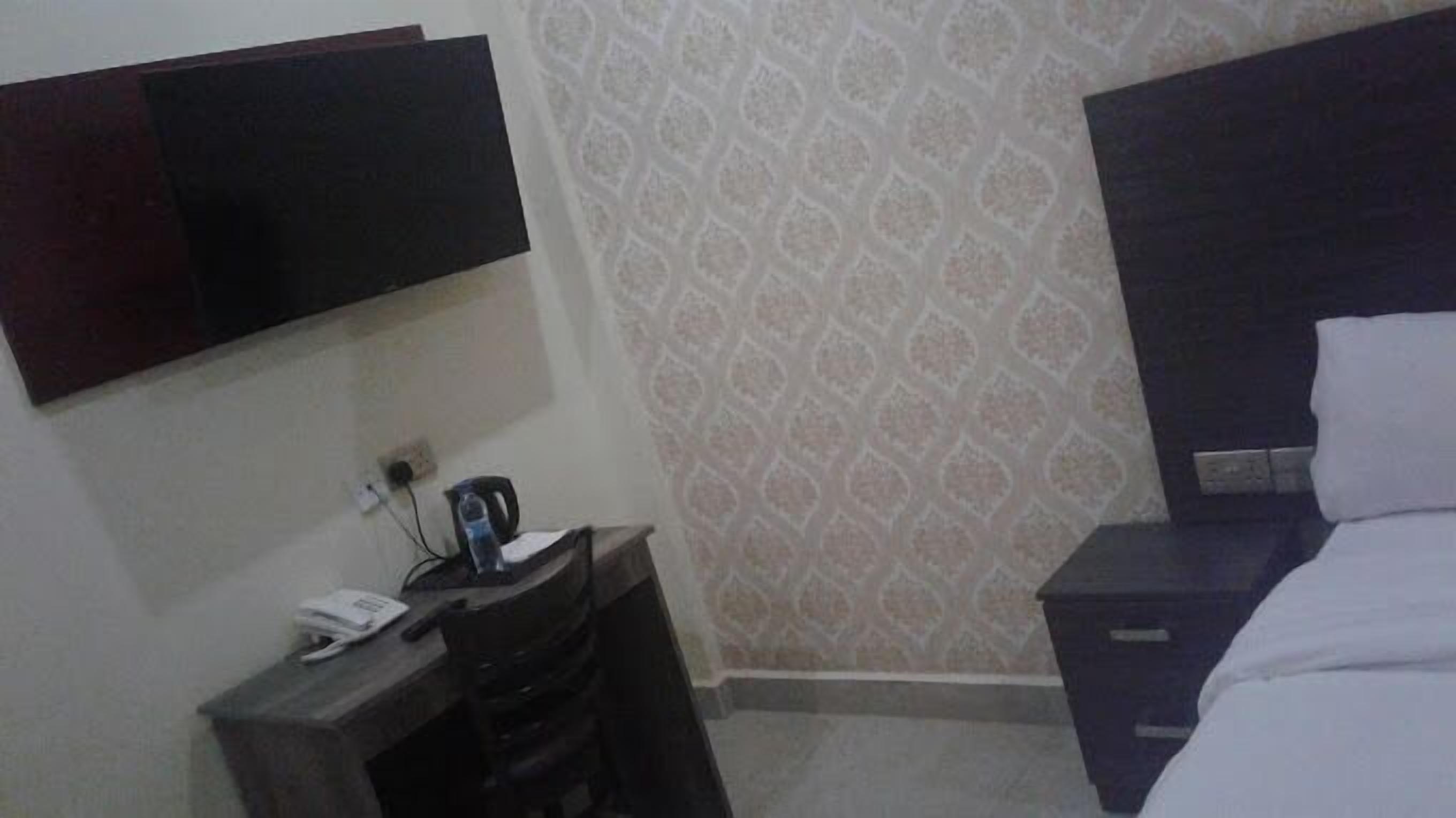 A hotel room with a flat-screen TV mounted on the wall, a desk with a telephone, and a bed with a dark headboard.