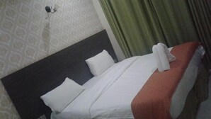A neatly made bed with white bedding and a red accent, a dark headboard, and a patterned wall. - The Junction Hotel & Suites (Kisii)