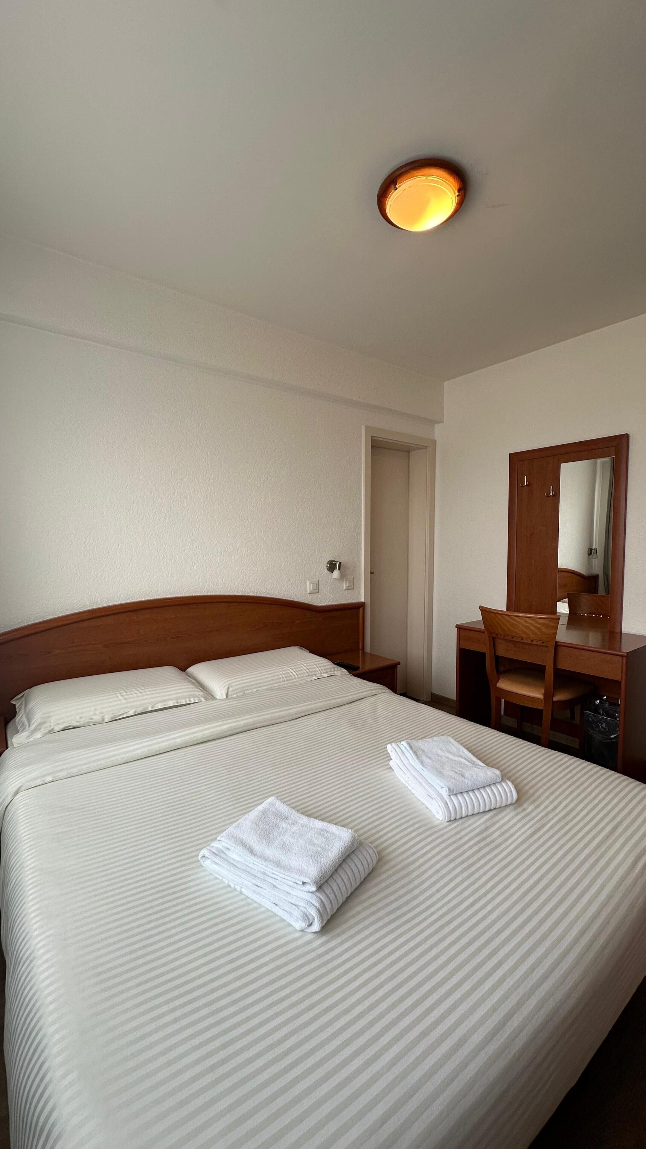 A hotel room with a large bed, a wooden dresser, a mirror, and a ceiling light.