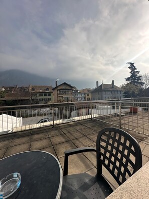 A terrace with a table and chairs, a white tent, and a view of buildings and a mountain in the background. - Hôtel du Quai  (Villeneuve)