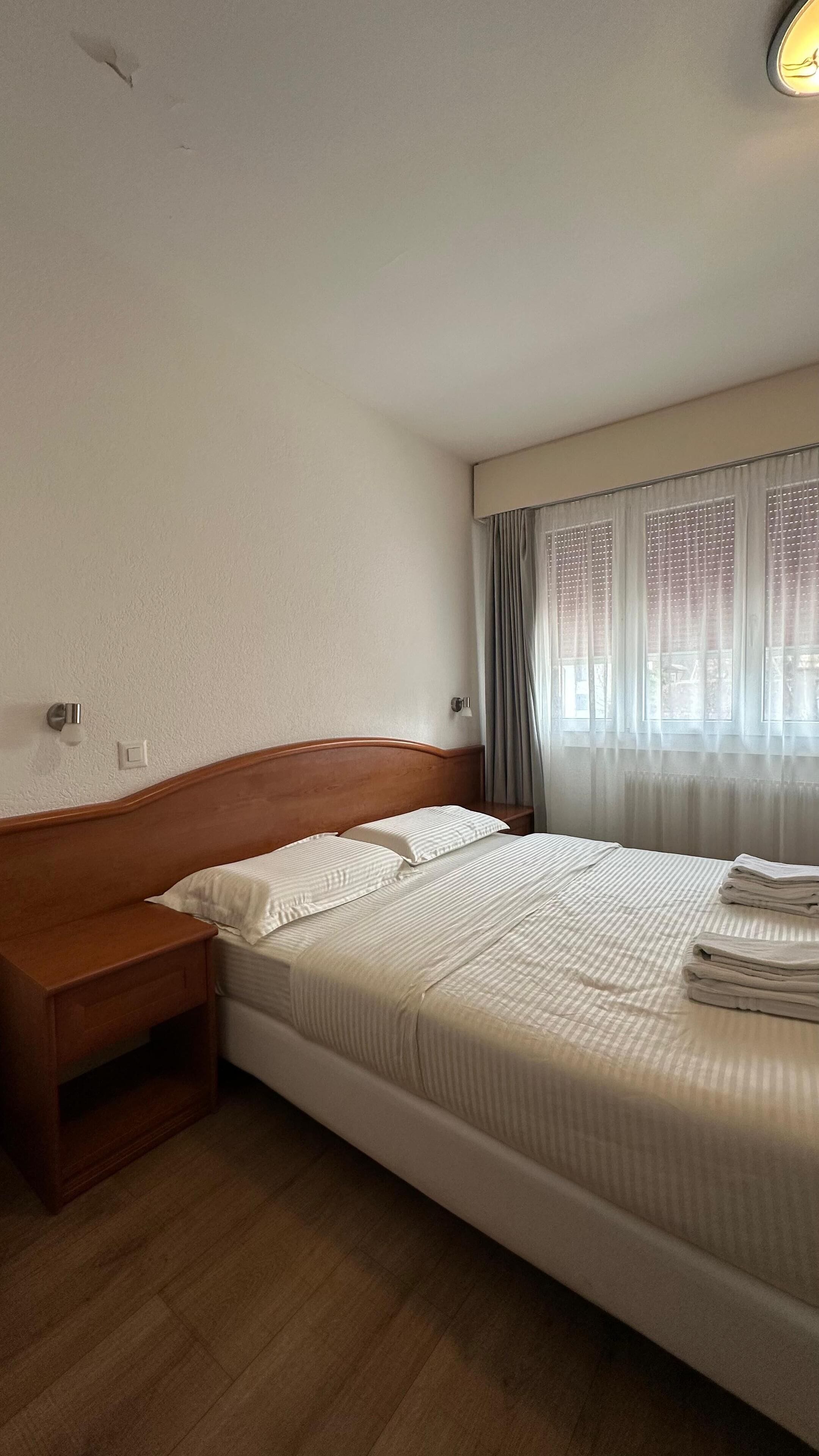 Un letto singolo con una testiera in legno, un comodino e una finestra con tende.