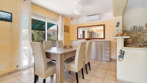 A dining area with a wooden table and four chairs, a kitchen with a tiled backsplash, and a large mirror above the counter.