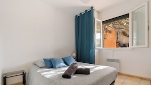 A bedroom with a bed, blue curtains, a window, and a radiator.