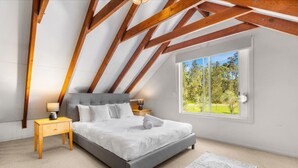 Camera da letto con soffitto spiovente, un letto, un comodino, una lampada, una finestra che si affaccia sul verde e un tappeto a motivi.