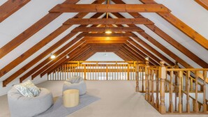 Una stanza mansardata con soffitto spiovente, travi in legno e un corrimano in legno, con due sacchi di fagioli.
