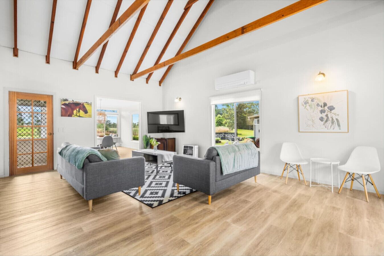 Un salon moderne avec deux canapés gris, un plafond en bois, un téléviseur et un mur blanc orné d’un tableau encadré.