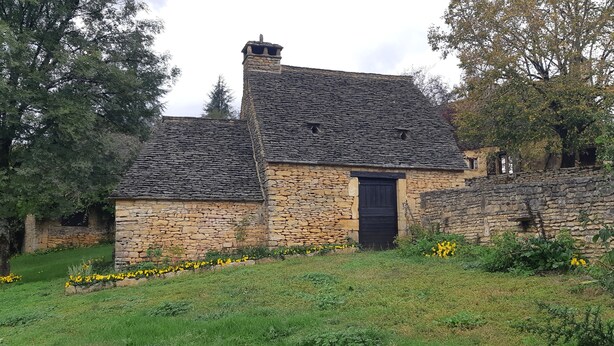 A stone building with a black door, surrounded by greenery and yellow flowers. - Typical Périgord Noir house with private pool (Saint-Geniès)