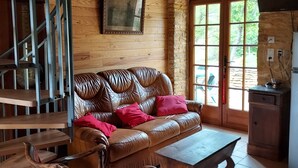 A rustic cabin interior with a wooden staircase, a leather sofa with red cushions, a wooden coffee table, and a patterned chair. - Typical Périgord Noir house with private pool (Saint-Geniès)