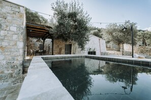 Un edificio de piedra con piscina, mobiliario exterior y olivos.
