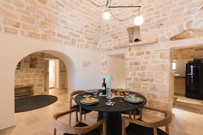 A dining area with a stone wall, a round table with chairs, and a chandelier. - Casale Palazzina Tommaso con Piscina (Fasano)