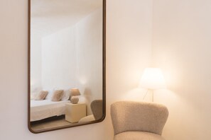 Un dormitorio con cama, mesita de noche, lámpara y una silla.