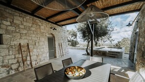 An outdoor patio with stone walls, a table with chairs, a bowl of fruit, and a view of the countryside. - Casale Palazzina Tommaso con Piscina (Fasano)