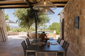 An outdoor dining area with a stone wall, a wooden table set with plates and cups, and a hanging light fixture. - Casale Palazzina Tommaso con Piscina (Fasano)
