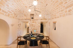 A dining area with a round table set for four, surrounded by stone walls and a vaulted ceiling.