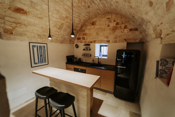 Una cocina con una isla de madera, taburetes negros, un refrigerador negro y una lámpara colgante.