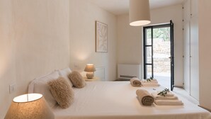 A bedroom with a large bed, a bedside table with a lamp, a wall-mounted air conditioner, and a view of the outdoors through a glass door. - Casale Palazzina Tommaso con Piscina (Fasano)