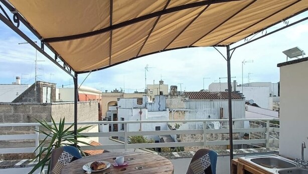 A rooftop terrace with a wooden table and chairs, a small sink, and a view of surrounding buildings. - Nardò historical center (Nardò)