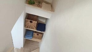 A corner of a room with a white wall, a wooden floor, and a shelf with wicker baskets and folded towels. - Nardò historical center (Nardò)
