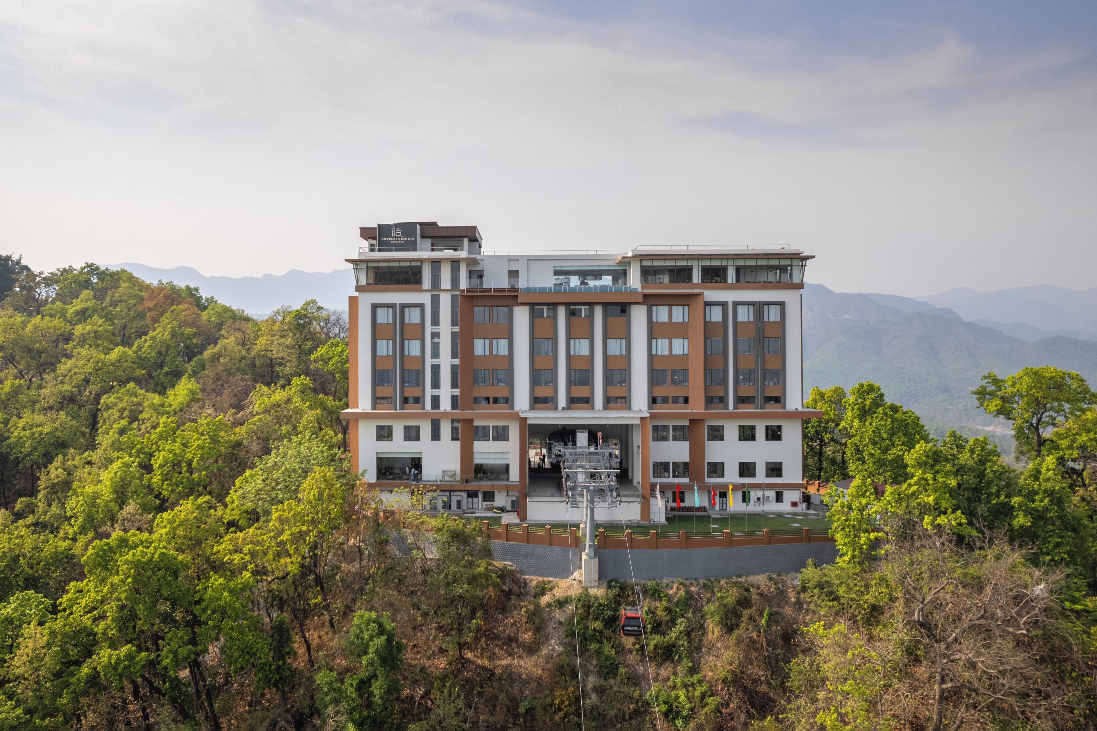Un hotel de varios pisos con un diseño arquitectónico moderno, que destaca por su entrada imponente y vistas panorámicas del paisaje montañoso circundante.