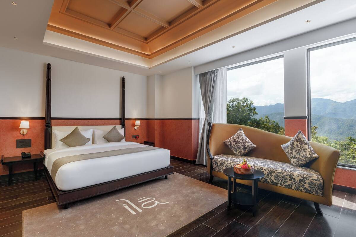 A hotel room with a bed, sofa, and large windows offering a mountain view.