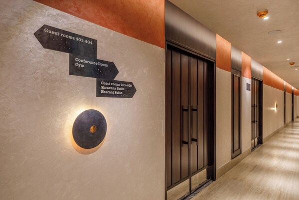 Un pasillo de hotel con indicaciones hacia habitaciones de huéspedes, salón de conferencias y gimnasio.
