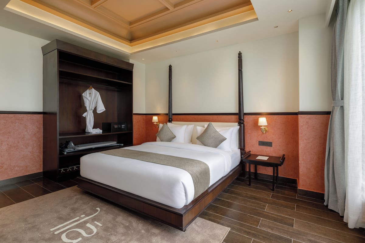 A hotel room with a large bed, a robe hanging on a shelf, a nightstand with a lamp, and a wooden headboard.
