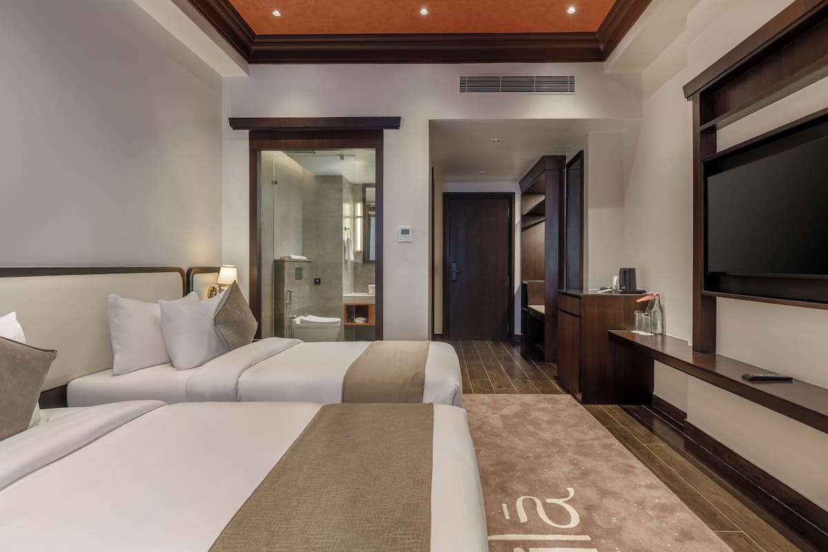A hotel room with two beds, a TV, a desk, and a bathroom visible through an open door.