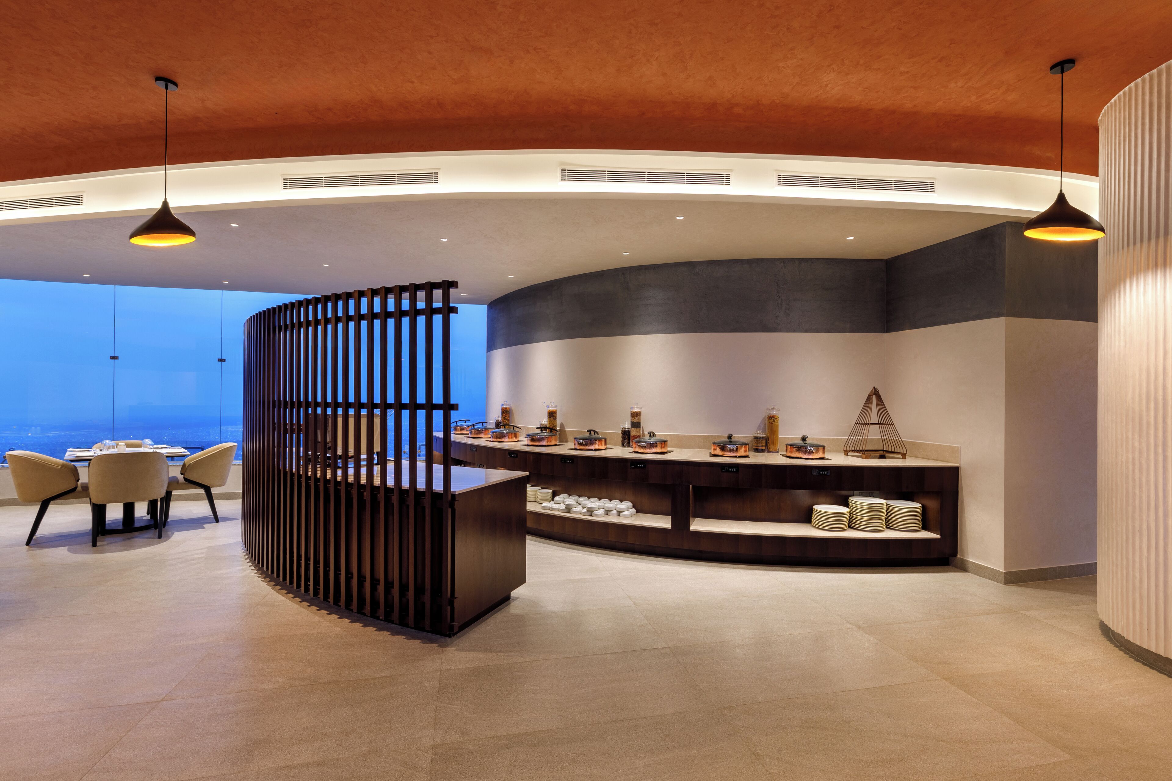 Un hall d’hôtel moderne avec un comptoir d’accueil incurvé, un espace salon et une vue sur le paysage urbain.