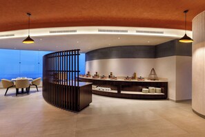 Un hall d’hôtel moderne avec un comptoir d’accueil incurvé, un espace salon et une vue sur le paysage urbain.