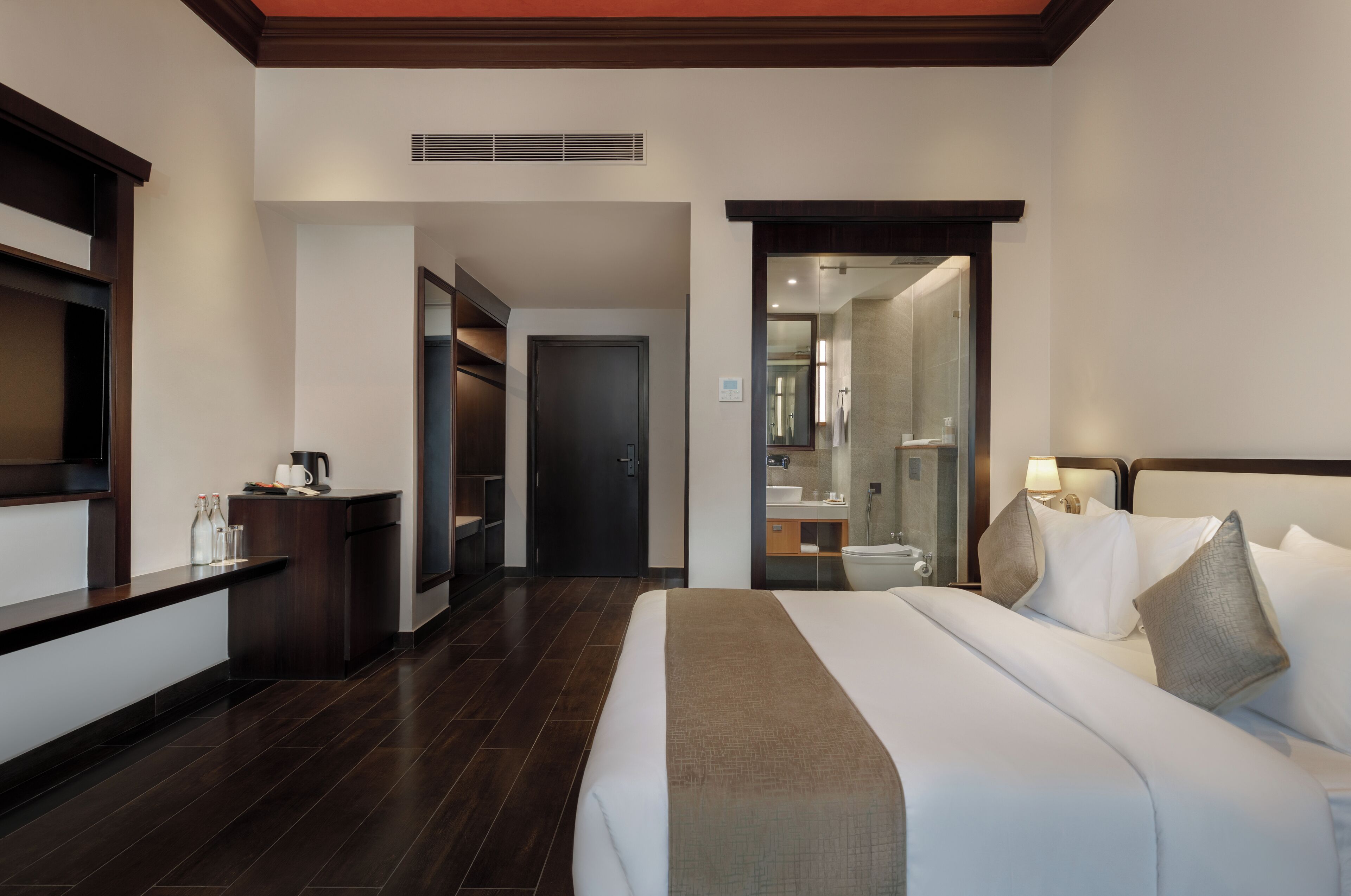 Una habitación de hotel con una cama grande, un escritorio con cafetera, un espejo y un baño visible a través de una puerta abierta.